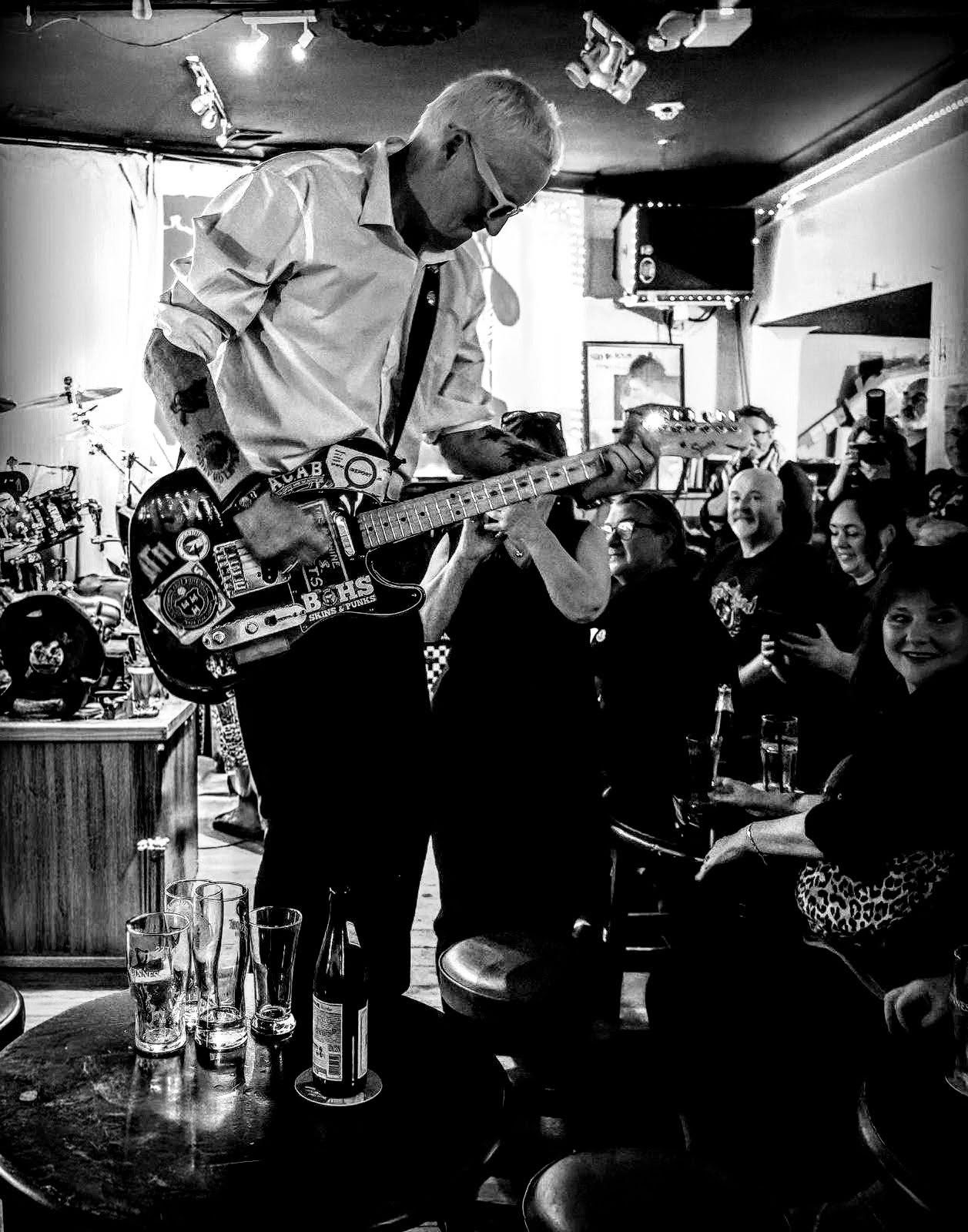 Bitzy playing guitar standing on a pub table in front of a packed crowd
